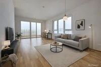 Wohnzimmer mit Couch, kleinem Tisch, Schreibtisch, Teppich, Sideboard mit Fernseher, Lampe,