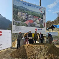Spatenstich von mehreren Personen mit Bautafel im Hintergrund
