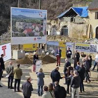 Bautafel mit Menschen Sandhügel mit Schaufeln und Helmen, sowie im Abbruch befindliche Häuser