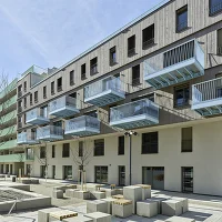 Wohnhaus mit Balkonen und Vorplatz mit Sitzblöcken.