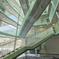 Offenes Stiegenhaus mit geschwungener Betontreppe, grünen Geländern und zentralem Innenhof.