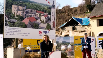 2 Personen mit Bautafel und im Abbruch befindliche Häuser